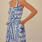 side view of model wearing blue and white title print romper with button front, smocked back, and tie waist