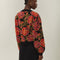 back view of model wearing black cropped cardigan with red and purple flowers, gold beading and gold decorative buttons