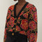 up close of model wearing black cropped cardigan with red and purple flowers, gold beading and gold decorative buttons