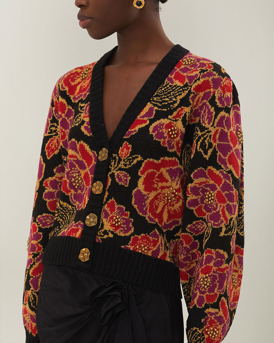 up close of model wearing black cropped cardigan with red and purple flowers, gold beading and gold decorative buttons