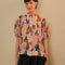 model wearing colorful abstract print with puff short sleeves, button front and ruffle across the bodice