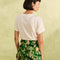 back view of model wearing nude shorts with tropical leaf print, bamboo belt, and white pepper tee