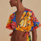 side view of model wearing blue cropped v-neck top with bold yellow, pink and red floral print and side ties