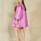 backview of model wearing metallic lavender dress with flowy skirt, oversized sleeves and collar and large red bow on the front