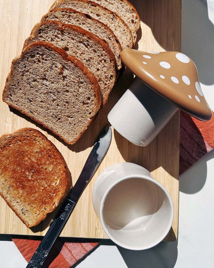 tan mushroom shaped utter storage container on a board with sliced bread