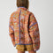 back view of model wearing colorful floral quilted jacket with periwinkle piping and trim