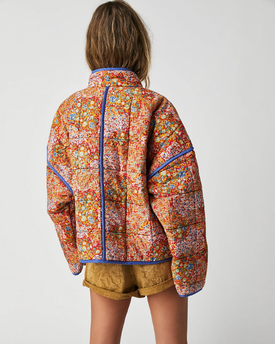 back view of model wearing colorful floral quilted jacket with periwinkle piping and trim