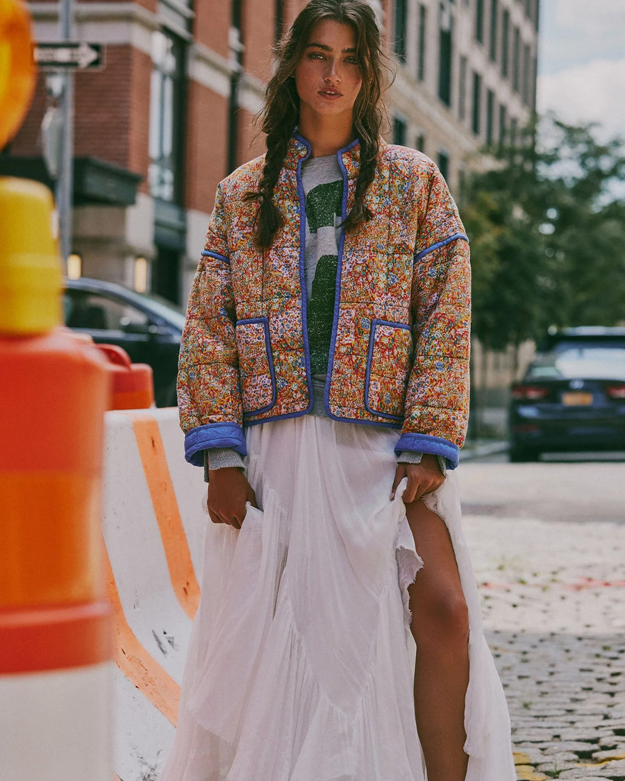 model wearing colorful floral quilted jacket with periwinkle piping and trim and white flowy skirt