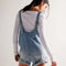 back view of model wearing light denim shortalls with patch front pockets and adjustable straps