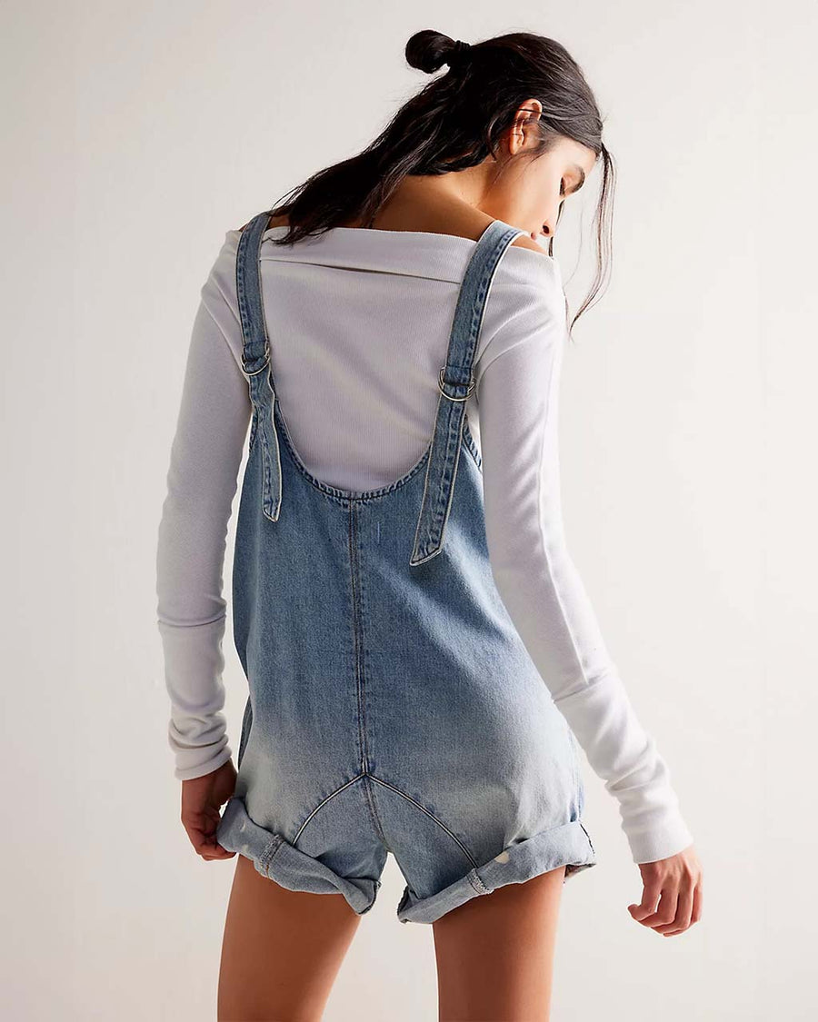 back view of model wearing light denim shortalls with patch front pockets and adjustable straps