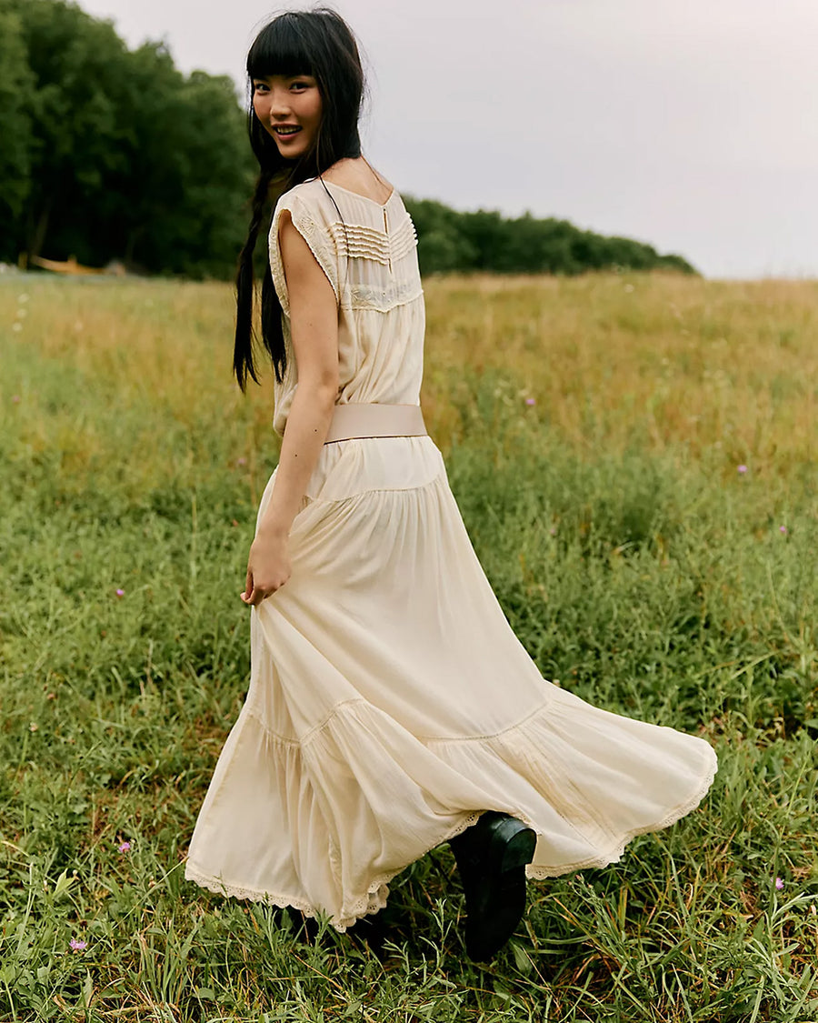 back view of model wearing cream shapeless maxi dress with intricate tank top sleeves, tiered skirt with various lace detail 