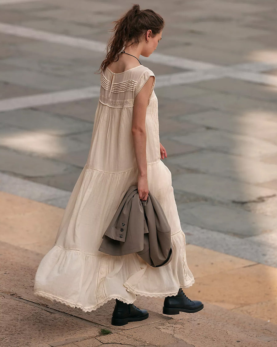 back view of model wearing cream shapeless maxi dress with intricate tank top sleeves, tiered skirt with various lace detail 