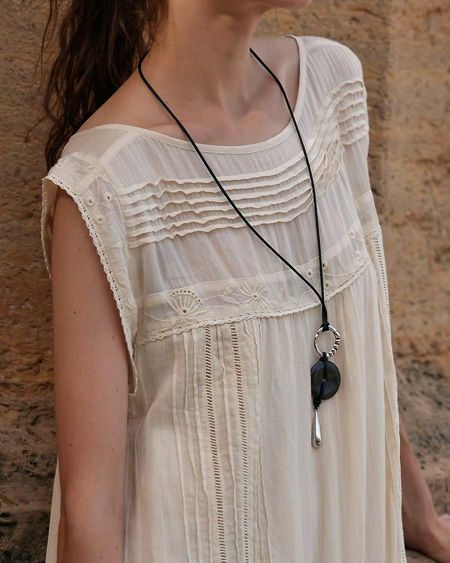 up close of model wearing cream shapeless maxi dress with intricate tank top sleeves, tiered skirt with various lace detail 