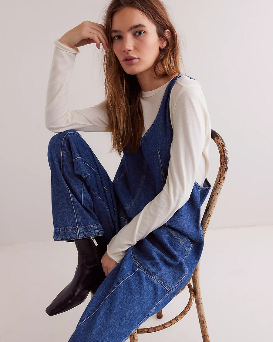 model sitting and wearing dark wash relaxed fit jumpsuit with front seaming and front patch pockets