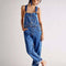 model wearing medium blue overalls with front pockets, adjustable straps and side button openings