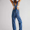 back view of model wearing medium blue overalls with front pockets, adjustable straps and side button openings