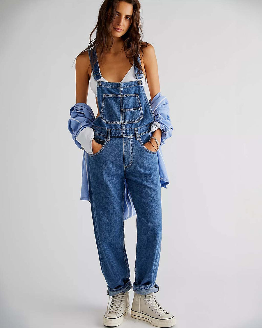 model wearing medium blue overalls with front pockets, adjustable straps and side button openings