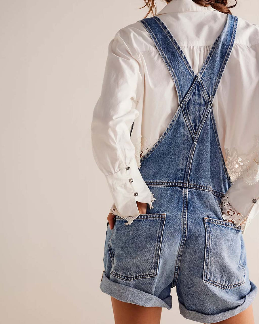 back view of model wearing medium denim shortalls with front pockets, adjustable straps and front pouch pocket at the bust 