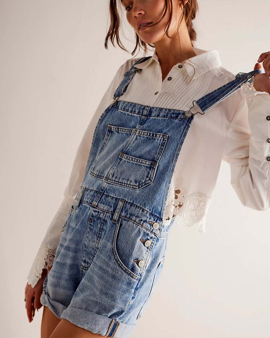 side view of model wearing medium denim shortalls with front pockets, adjustable straps and front pouch pocket at the bust 