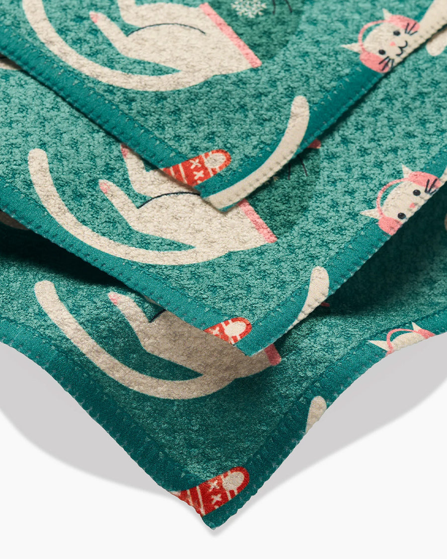 up close of set of 3 teal dishcloths with white cats in scarves, sweaters and christmas jammies