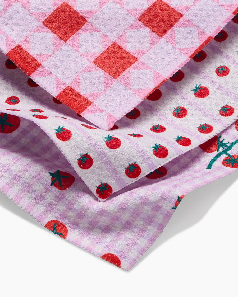 up close of set of three dish cloths: pink patchwork, tomato stripe, and tomato gingham