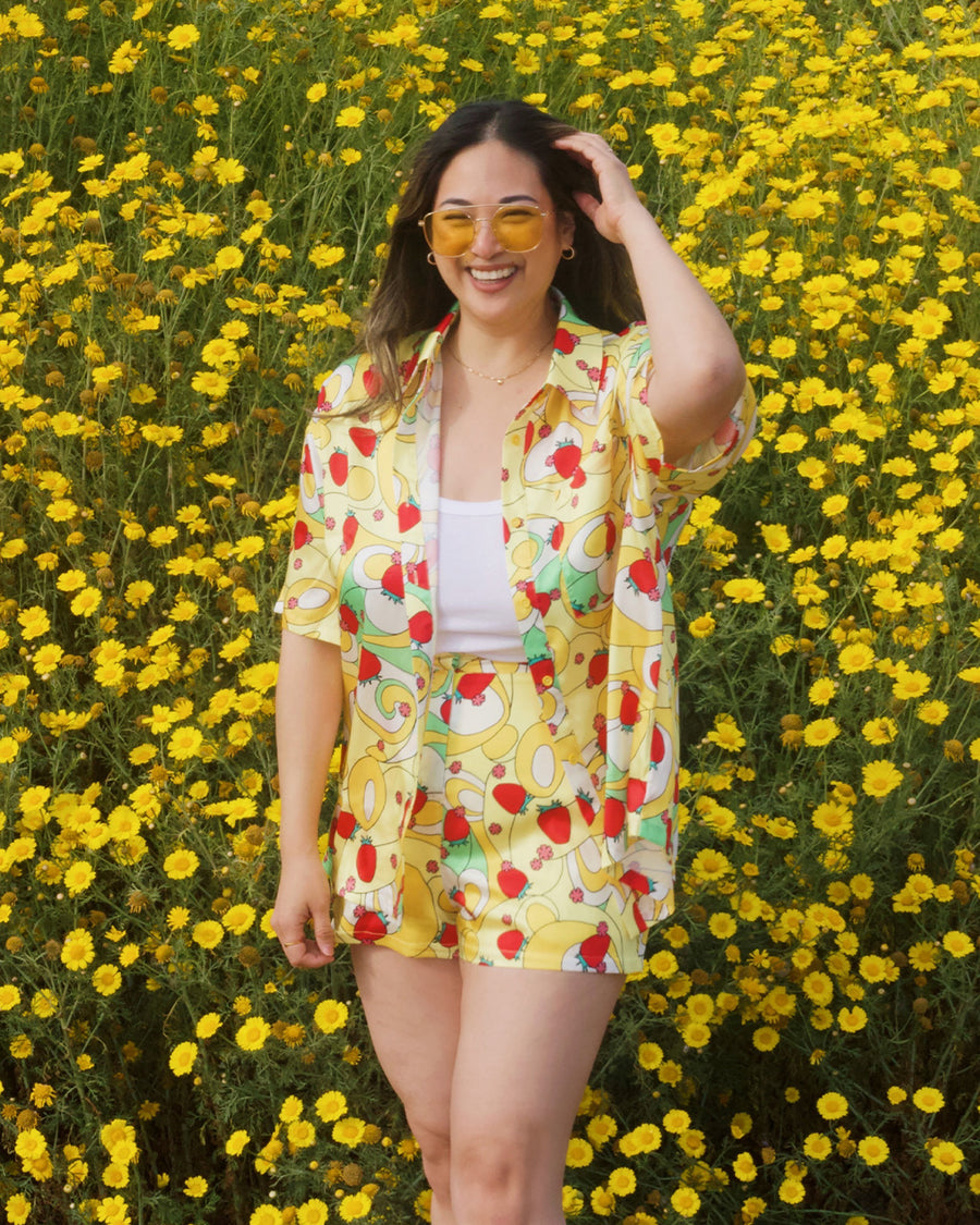 model wearing yellow trippy button down top with vibrant strawberry print and paired with matching shorts