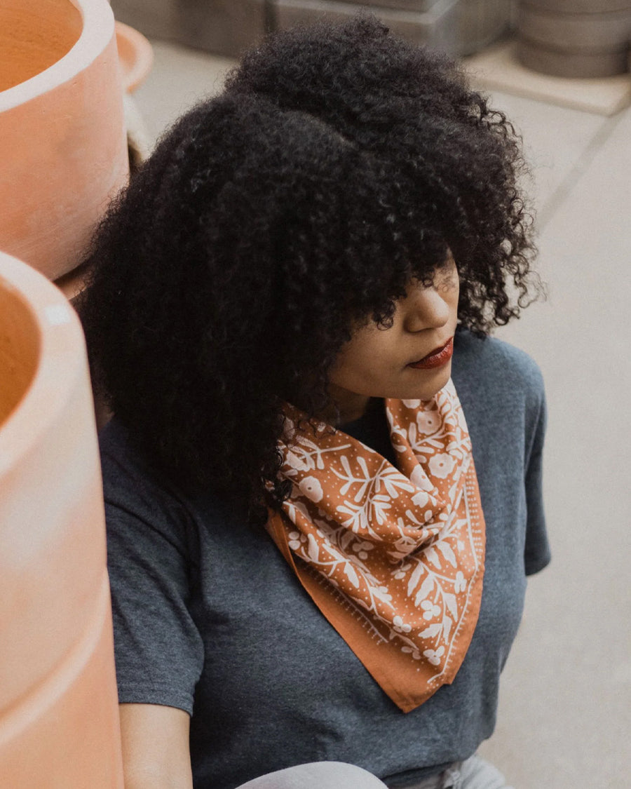 model wearing terracotta square bandana with light pink floral print around their neck