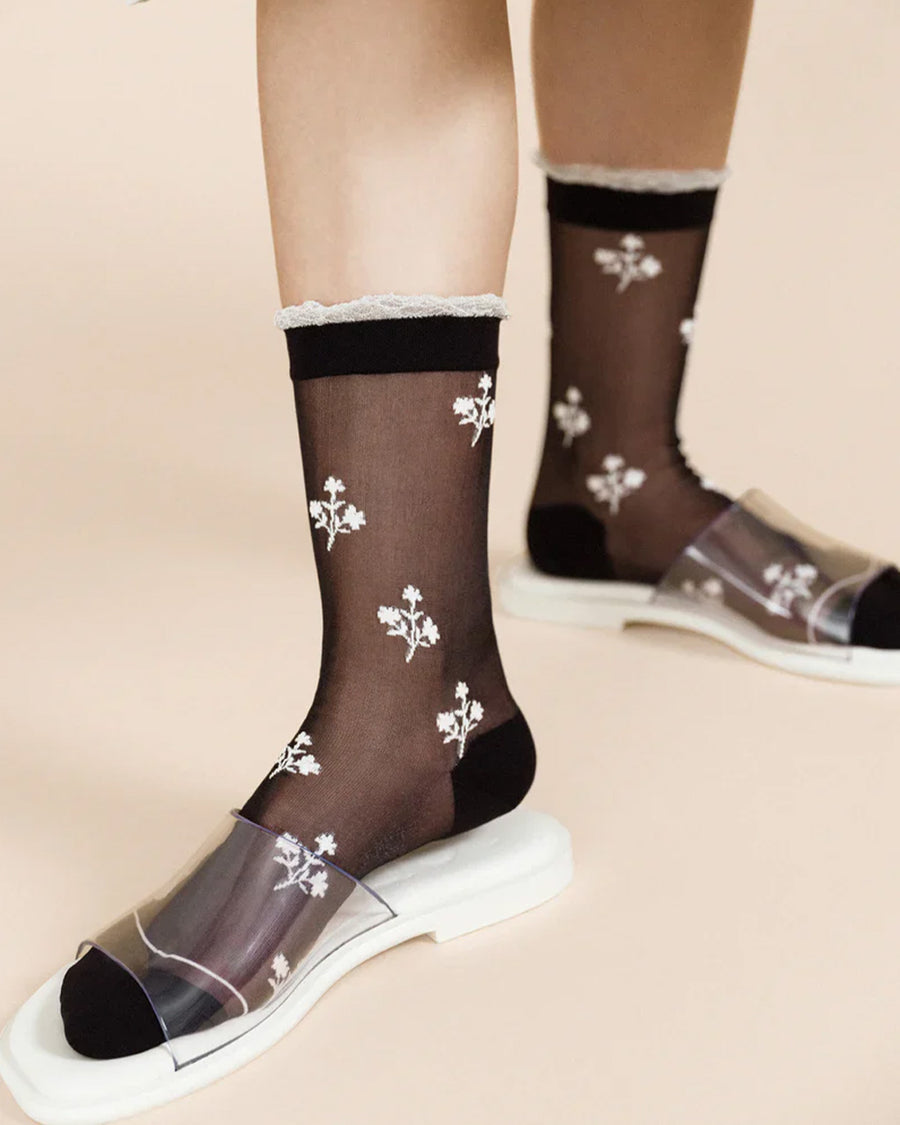 up close of model wearing black sheer socks with white trim and dainty white flowers