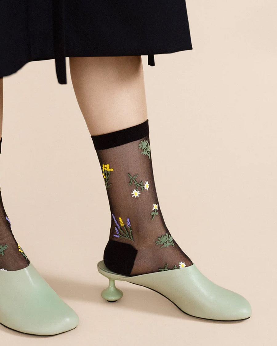 up close of model wearing black sheer socks with colorful wildflower print