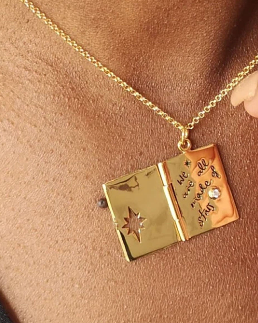 model wearing gold locket necklace with celestial scene and says 'we are all made of stars' inside