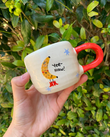 white coffee mug with red handle and 'yee-haw' banana graphic