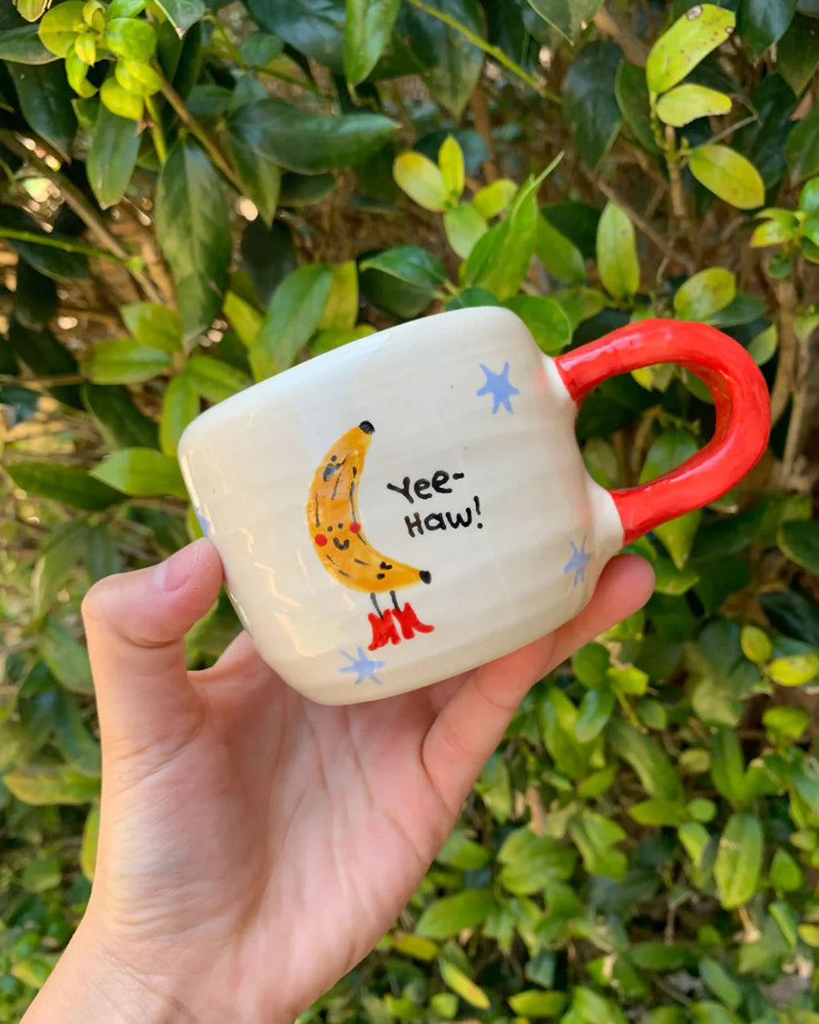 white coffee mug with red handle and 'yee-haw' banana graphic