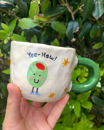 model holding white mug with green handle with 'yee-haw' light green olive on it