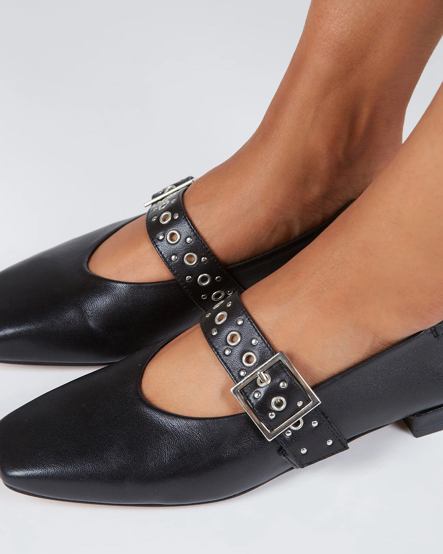 up close of model wearing black mary jane flats with elastic back and thick buckle strap with silver grommets and buckle