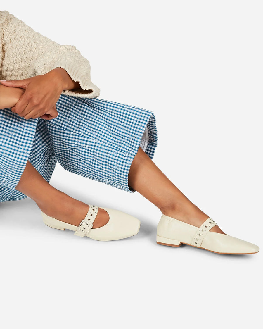 model wearing creme mary jane flats with elastic back and thick buckle strap with silver grommets and buckle