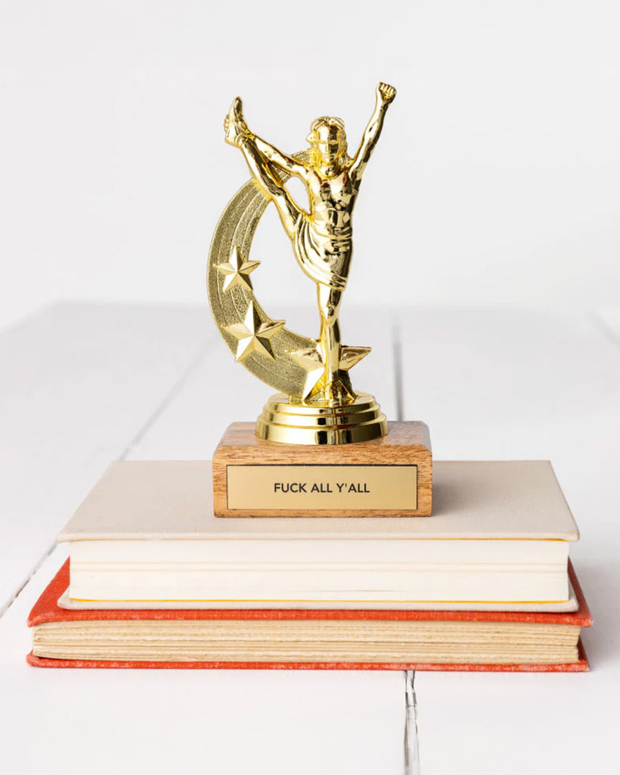 'f*ck all y'all' gold trophy on a stack of books