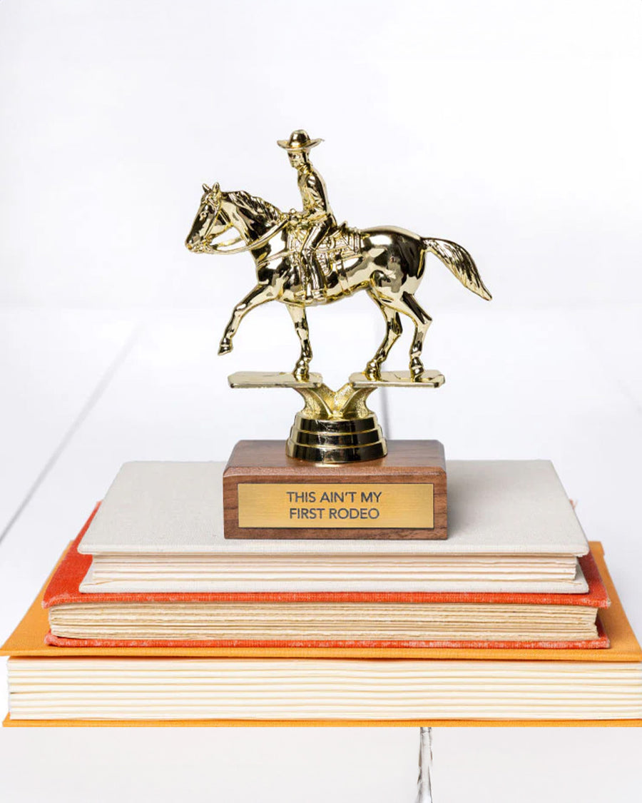 'this ain't my first rodeo' gold trophy on a stack of books