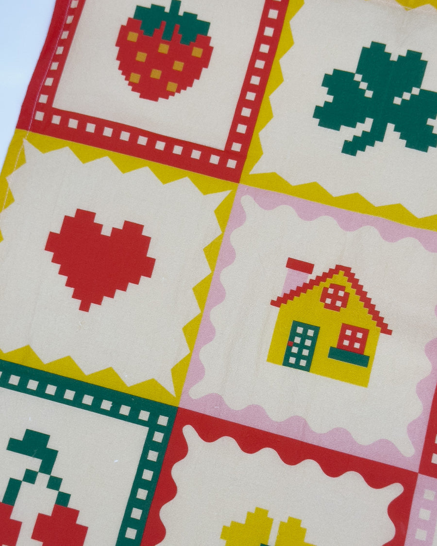 up close of cream tea towel with strawberry, shamrock, banana, heart, house, pretzel, cherry, flower and bow icons