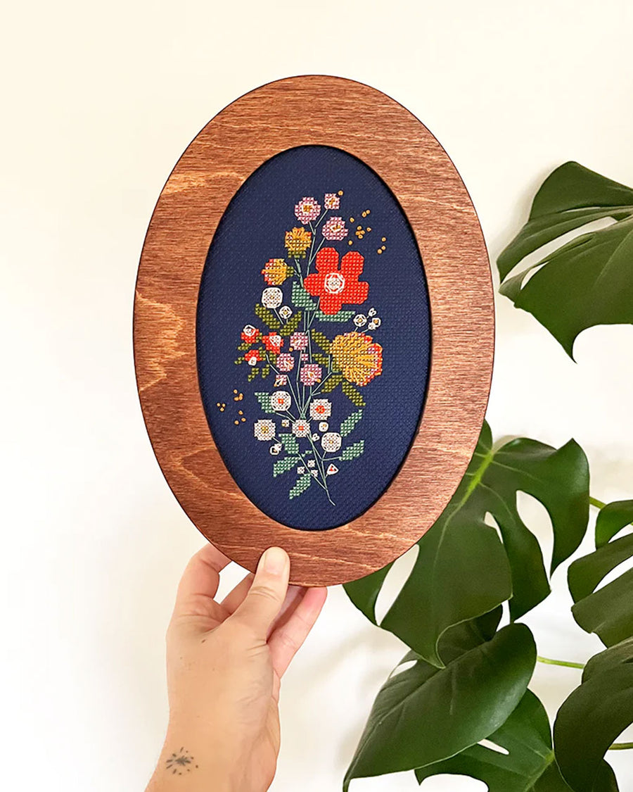 model holding blue cross stitch kit with colorful flowers in frame