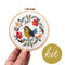 model holding white embroidered cross stitch kit with yellow and black bird surrounded by flowers 