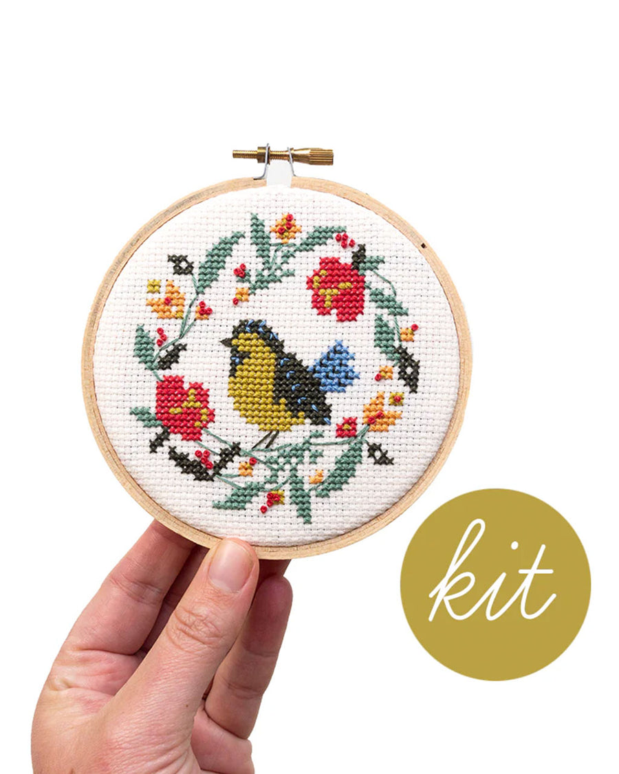 model holding white embroidered cross stitch kit with yellow and black bird surrounded by flowers 