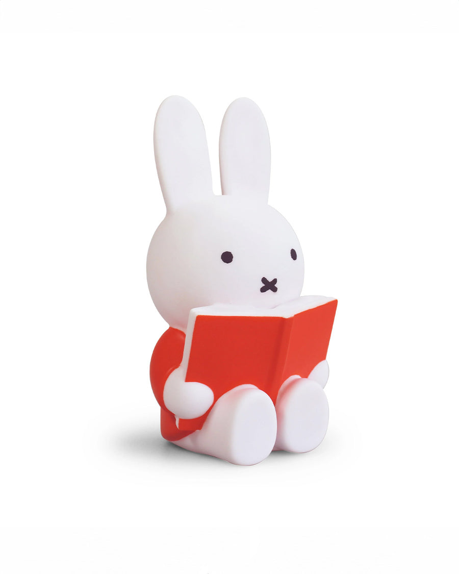 side view of medium miffy sitting and reading a red book