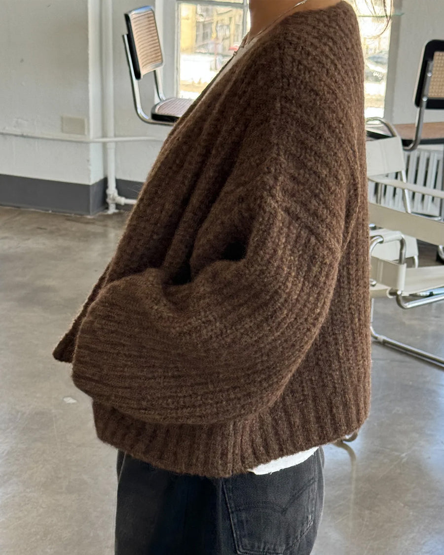 side view of model wearing dark brown chunky knit open front cardigan with front patch pockets