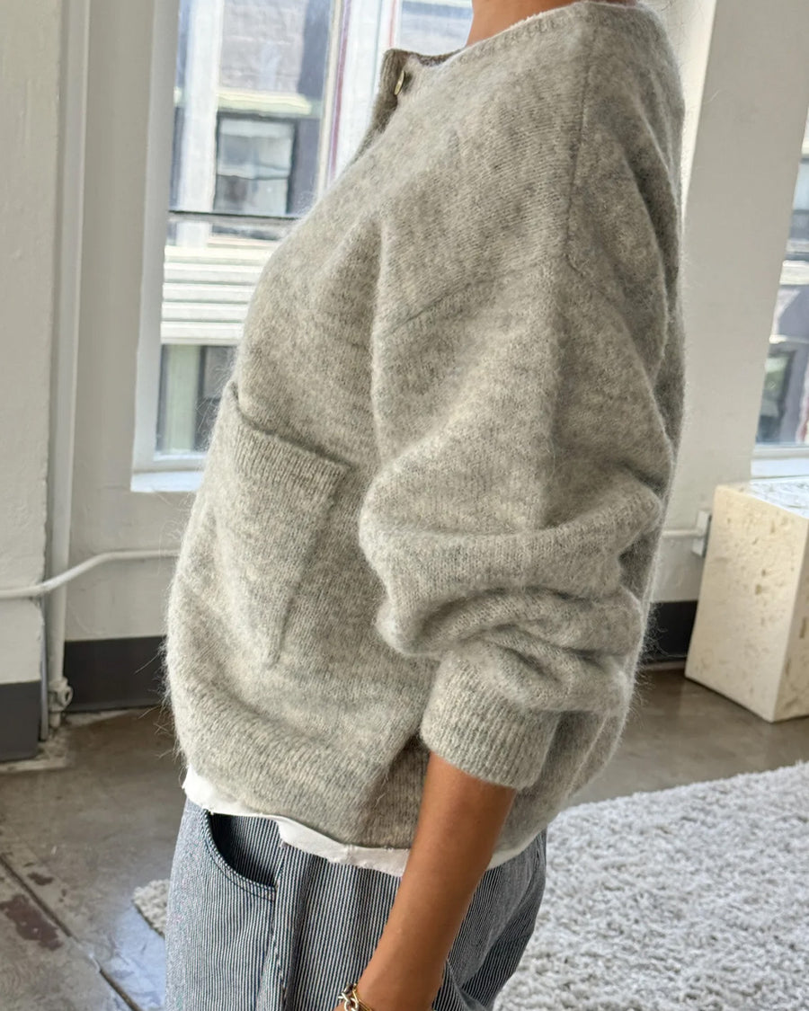 side view of model wearing light grey cardigan with white button front and front patch pockets