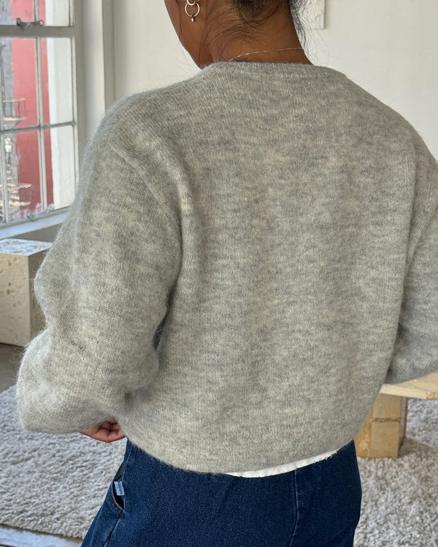 back view of model wearing light grey cardigan with white button front and front patch pockets