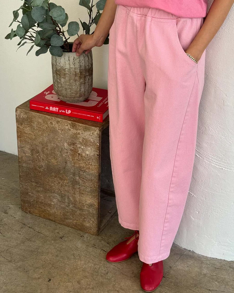 side view of model wearing bubblegum pink cotton pants with slight balloon legs and side pockets
