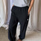 side view of model wearing black cotton balloon pants with elastic at ankles and side pockets