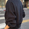 side view of model wearing black crewneck sweatshirt with drop sleeves and banded bottom