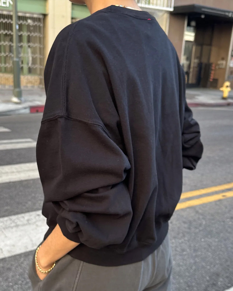 side view of model wearing black crewneck sweatshirt with drop sleeves and banded bottom