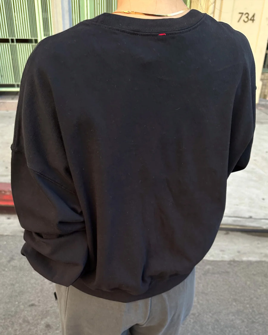 back view of model wearing black crewneck sweatshirt with drop sleeves and banded bottom